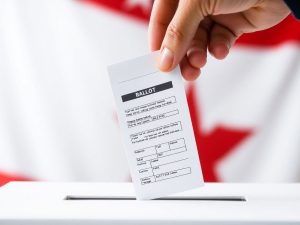 O mână ține un vot pe fundalul unui steag.